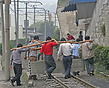 Workers manually lift a concrete beam over rail tracks. They will carr...