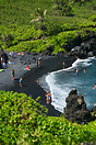 People enjoying the sun and surf of Honokalani black sand beach in the...