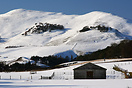 A wooden barn sits beneath the snow-covered Pentland Hills.